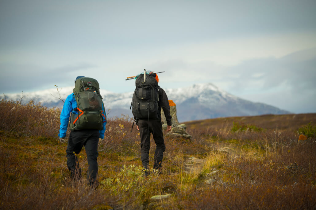 Ammarnäs, Aigert. Ryggen av två fjällvandrare med fjäll i bakgrunden.