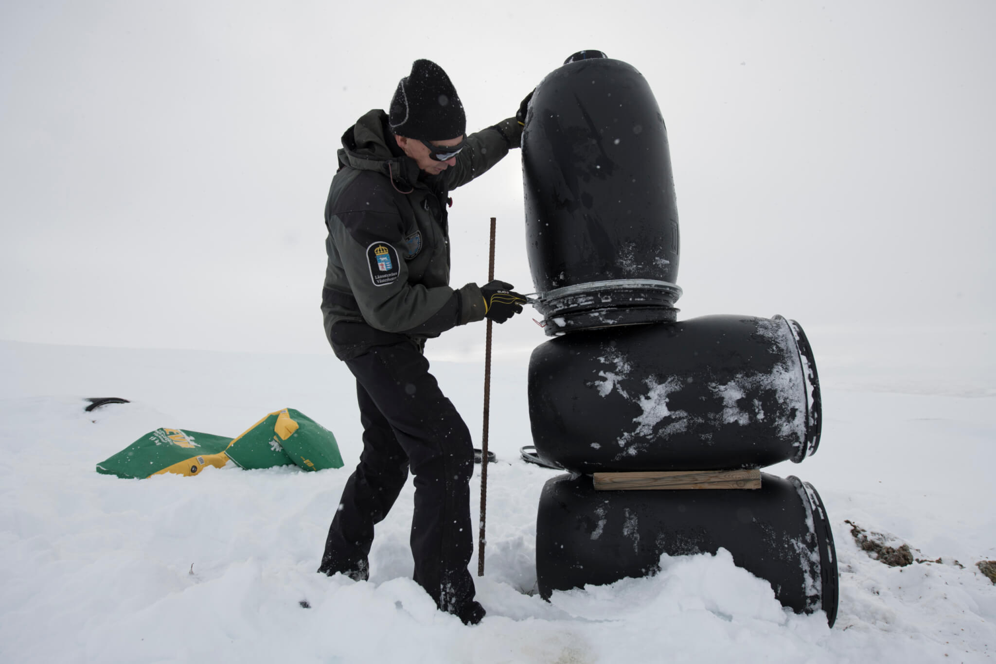 Man staplar svarta tunnor till en fjällrävsmatare.