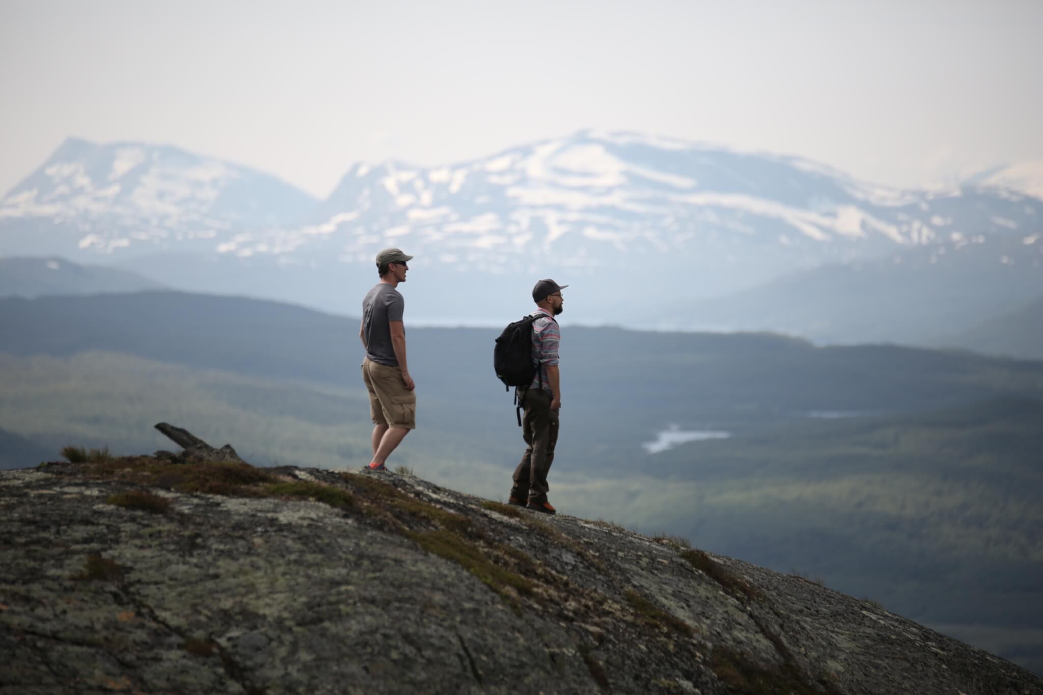 Två män står på ett fjäll och blickar till höger .