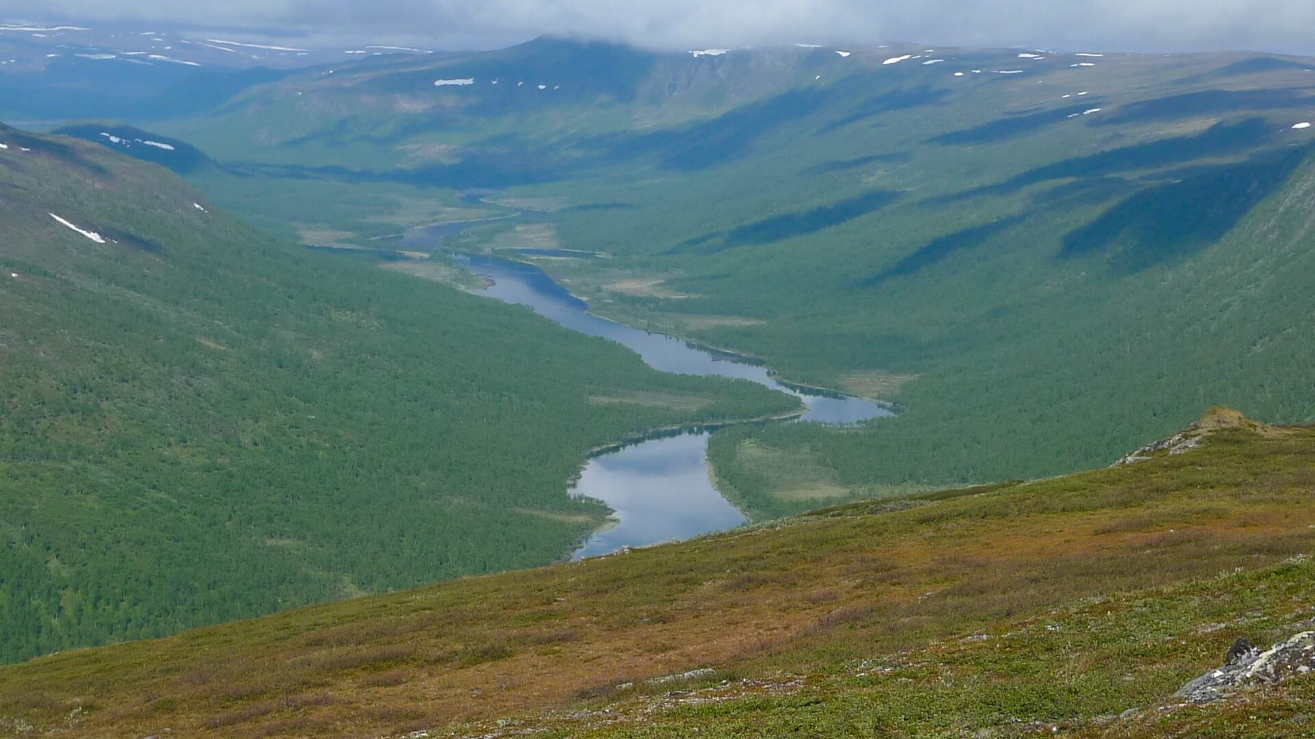 En älvdal syns från ovan. Moln skapar skuggor på vissa ställen i dalen.